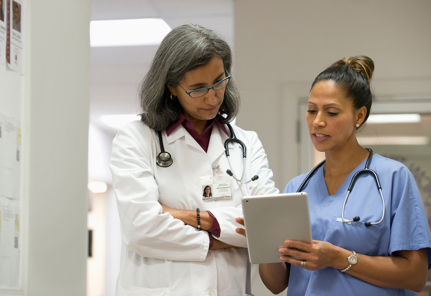 A female provider reviewing data with a female nurse while standing in a hospital hallway.